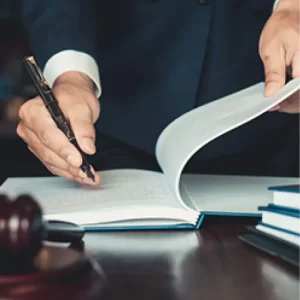 A person in a suit signs a document at a desk with a gavel and books.